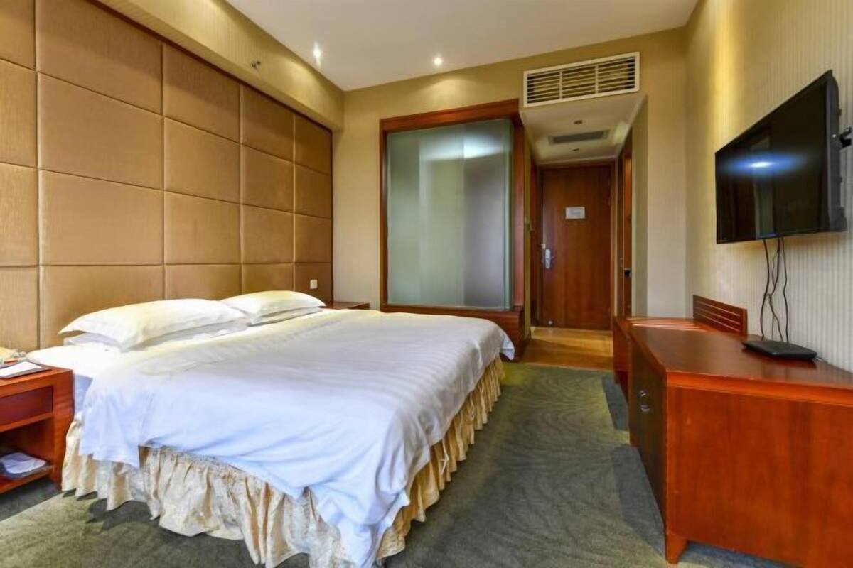 A hotel room with a bed, a desk, a television, and a sliding door leading to a bathroom.