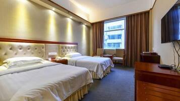 A hotel room with two beds, a desk, a chair, a TV, and a window with curtains.