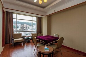 A hotel room with a large window, a bed with a purple cover, a small table, two chairs, and a view of buildings outside. - Wanghailou Hotel (Huizhou)