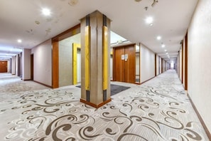 A hotel corridor with patterned carpet, wooden doors, and a central pillar. - Wanghailou Hotel (Huizhou)