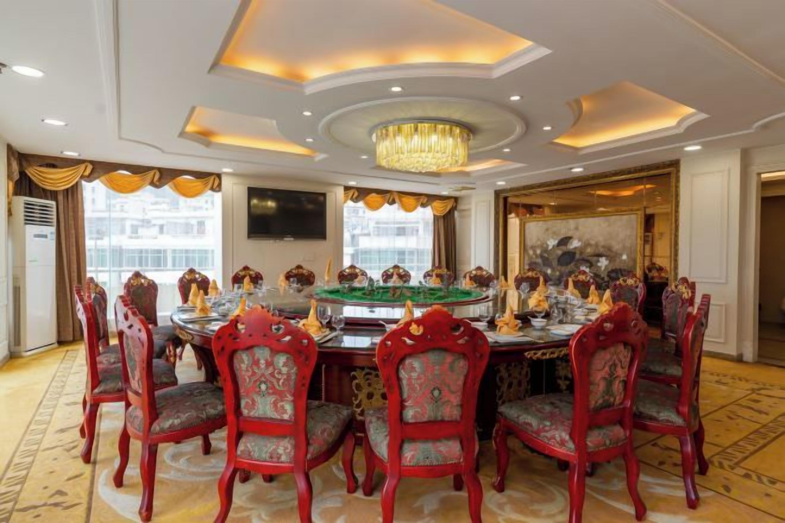 Uma sala de jantar formal com uma mesa redonda, cadeiras estofadas em vermelho e um candelabro.