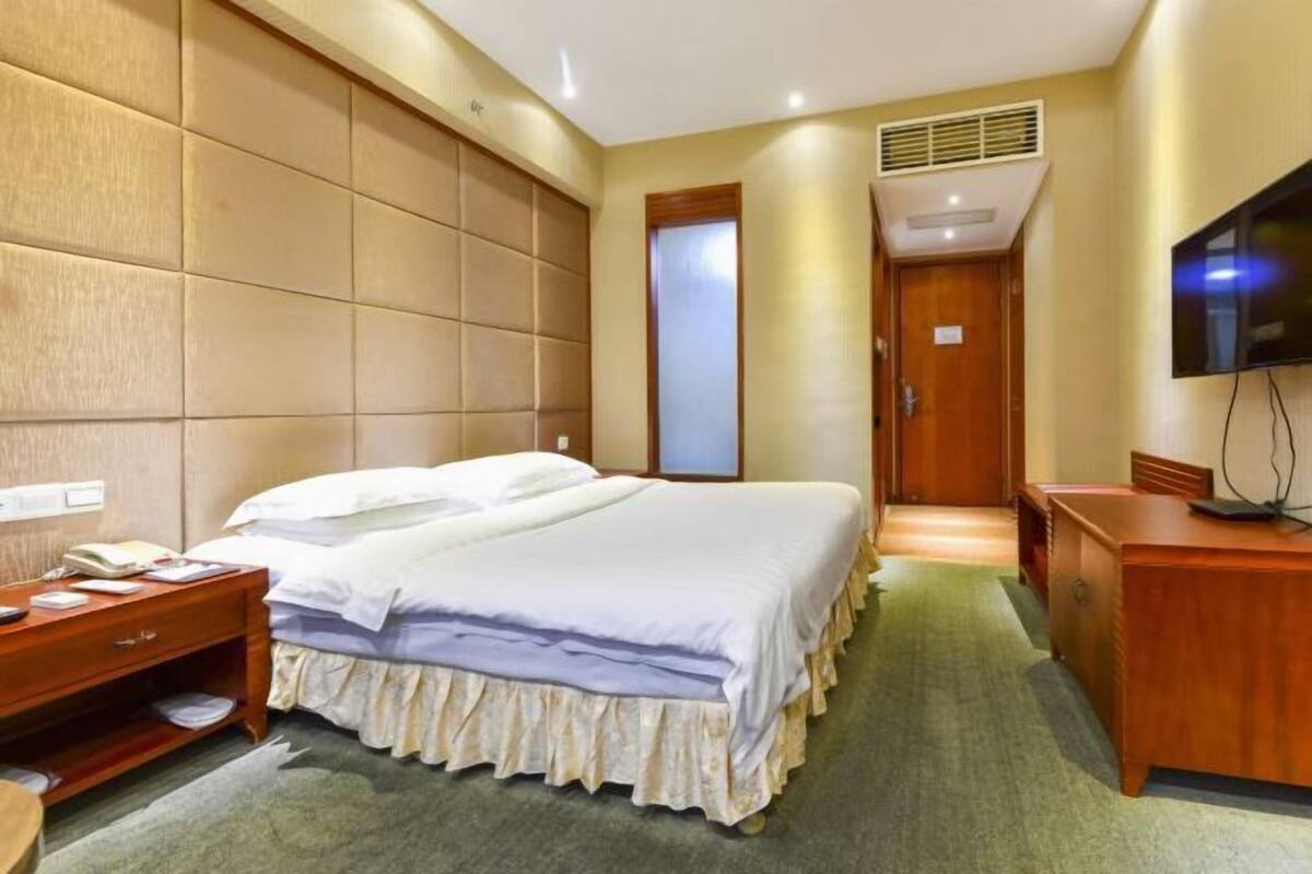 A hotel room with a large bed, a wooden dresser, a television, and a door leading to a hallway.