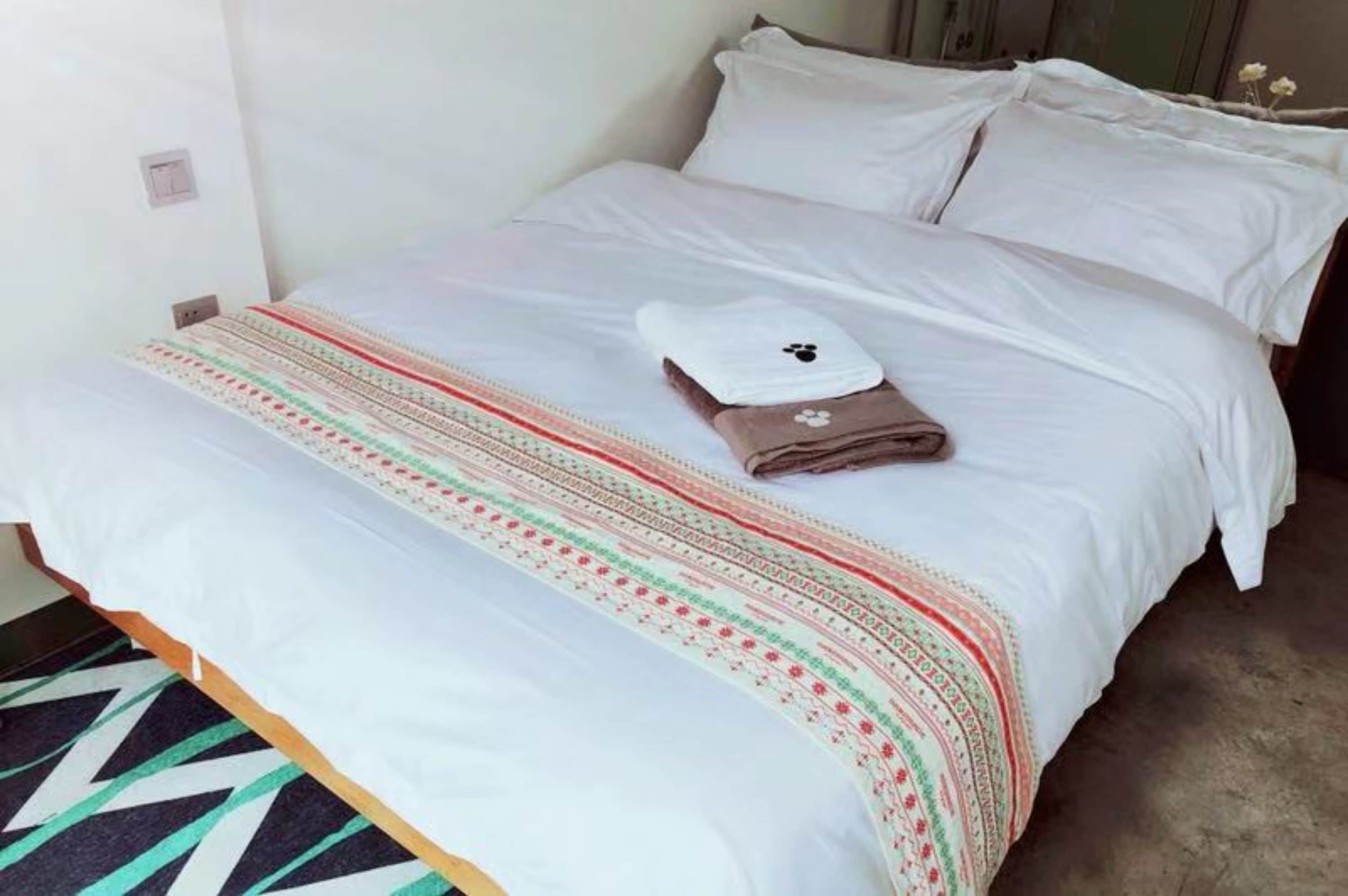 Uma cama bem arrumada com lençóis brancos, um cobertor estampado e duas toalhas com estampas de patas.