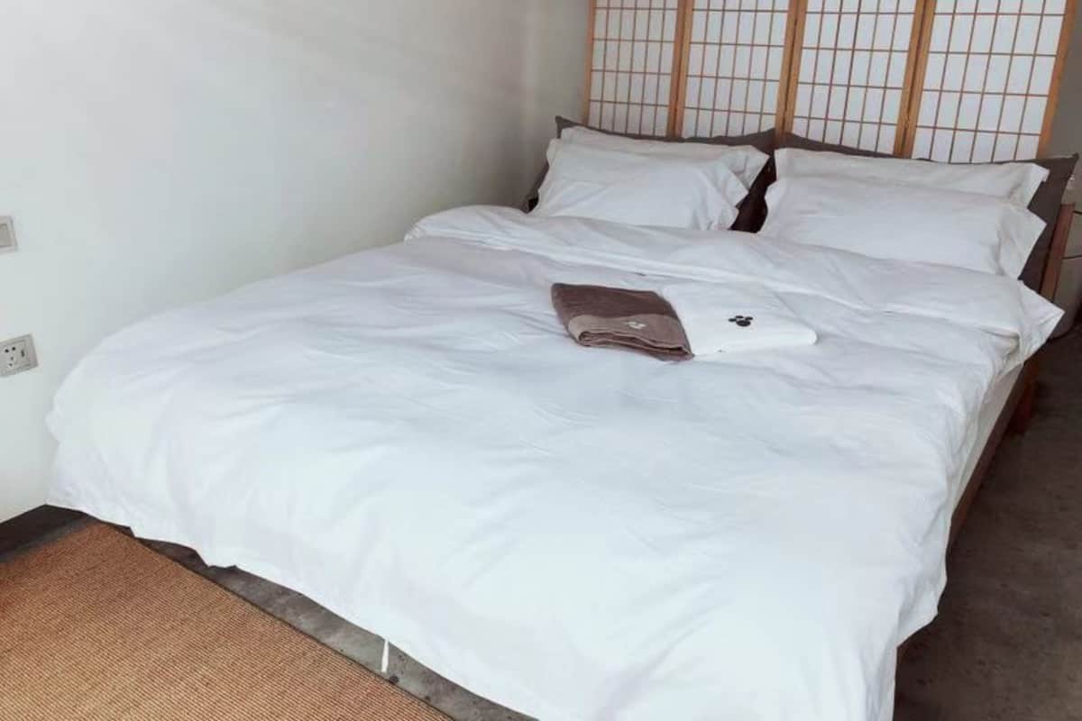 A neatly made bed with white bedding and a folded brown towel.