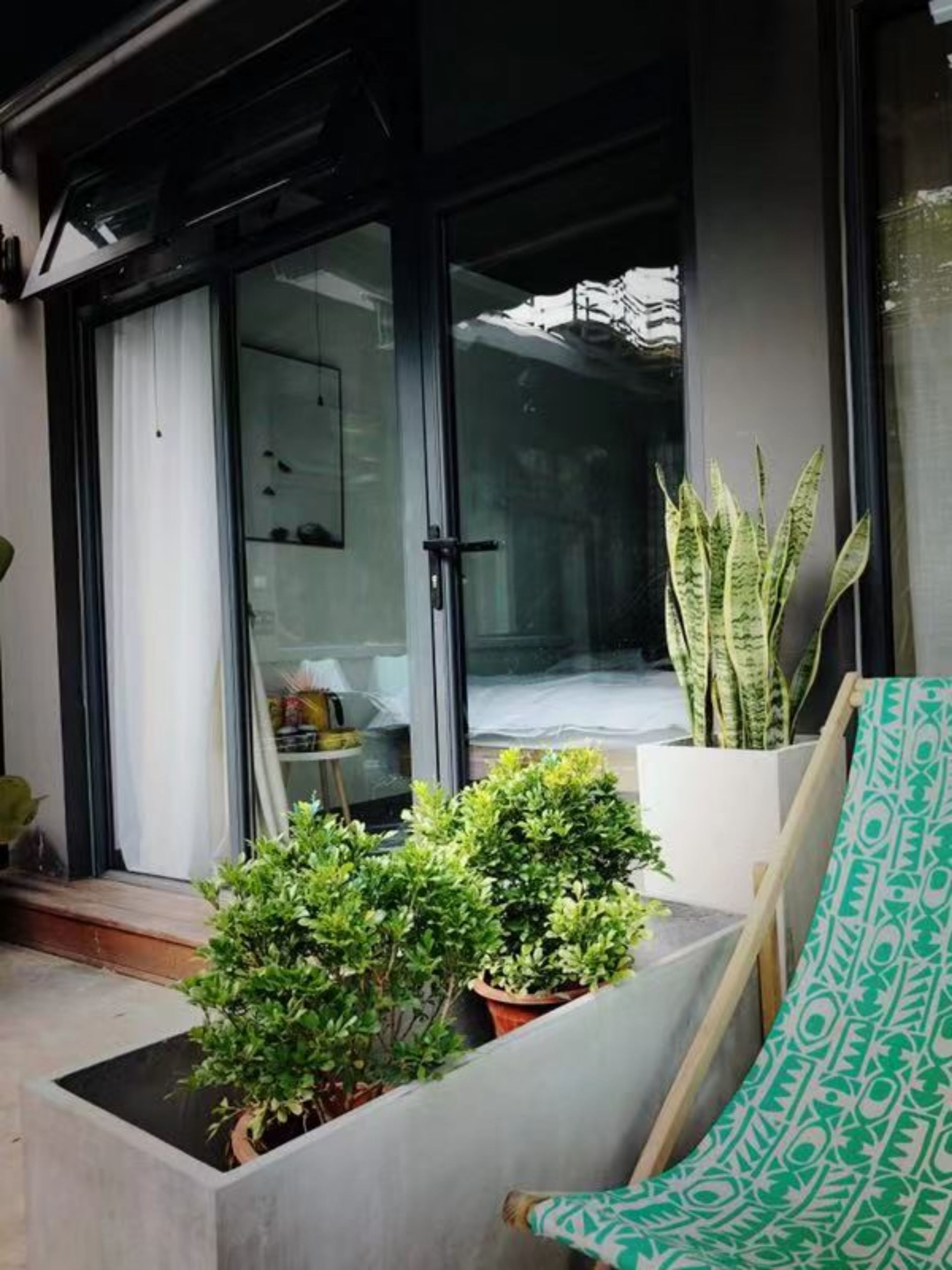 A modern patio with a sliding glass door leading to a living area, a potted plant, and a patterned cushion.