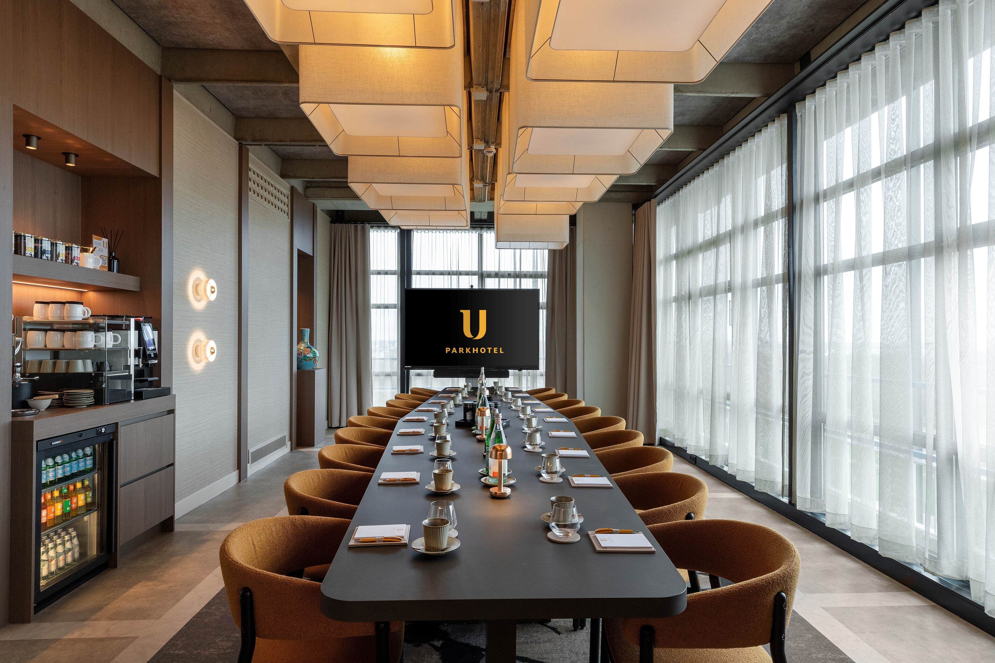 A conference room with a long table, chairs, a television screen, and a minibar.