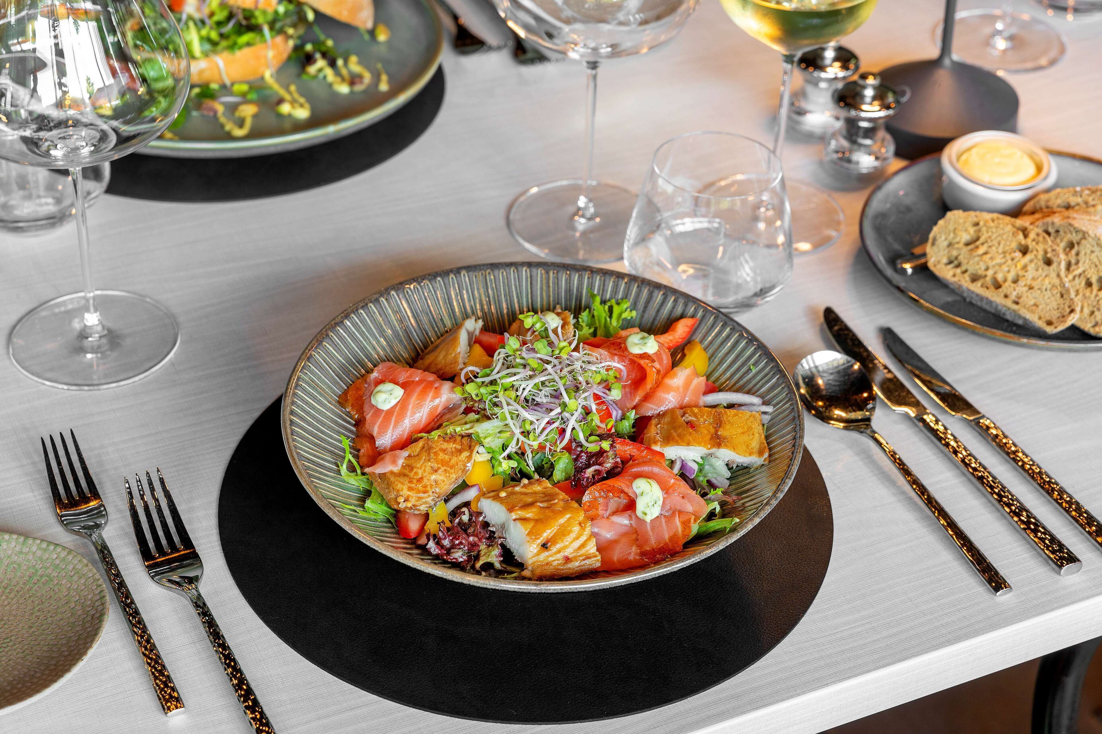 A dining table with a bowl of salad, cutlery, and glasses of wine.