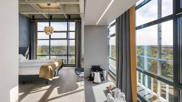 Habitación de hotel moderna con una cama grande, un escritorio con cafetera y vistas a la ciudad.