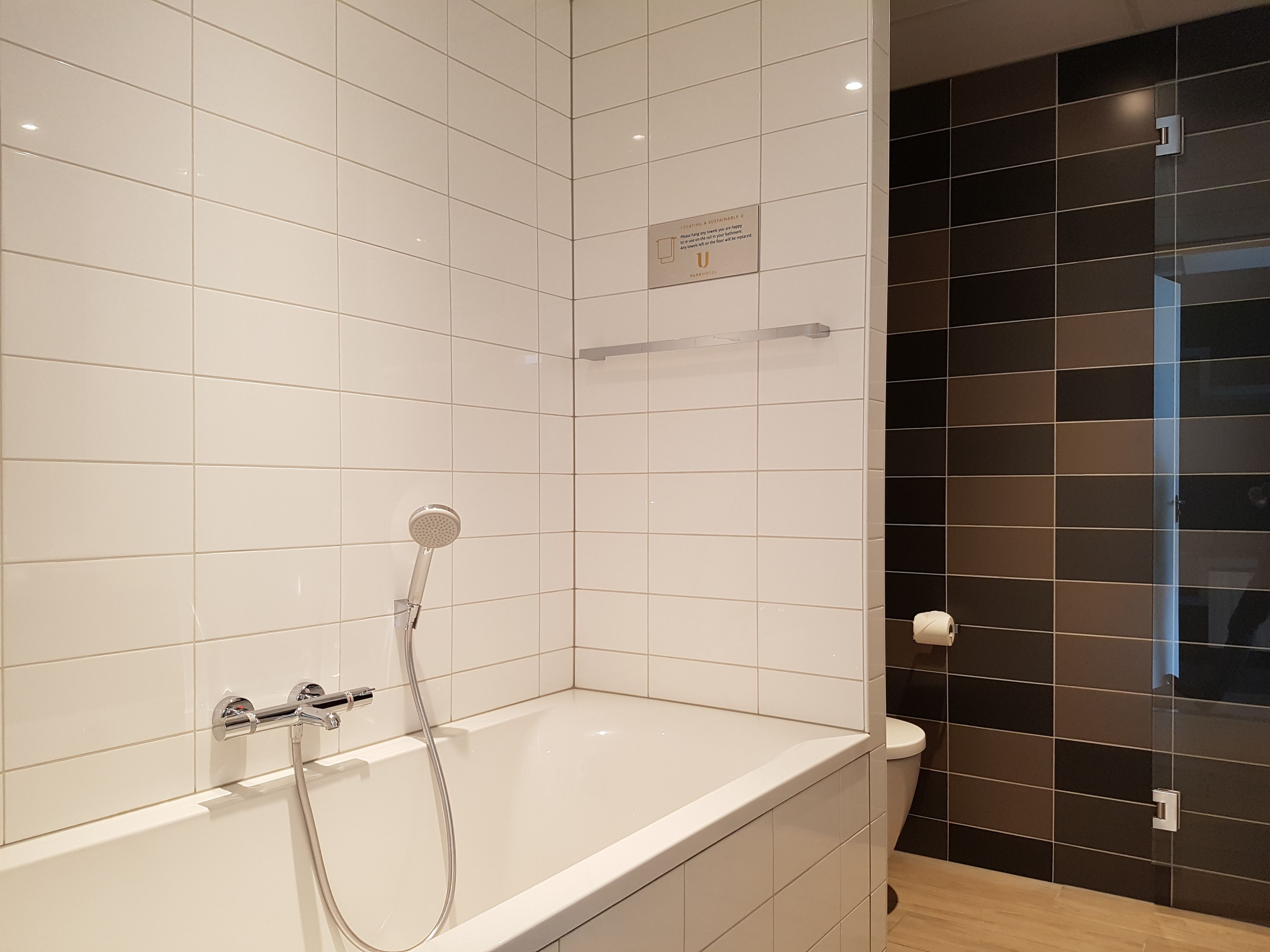 Un baño moderno con azulejos blancos, una bañera, un cabezal de ducha y un inodoro.
