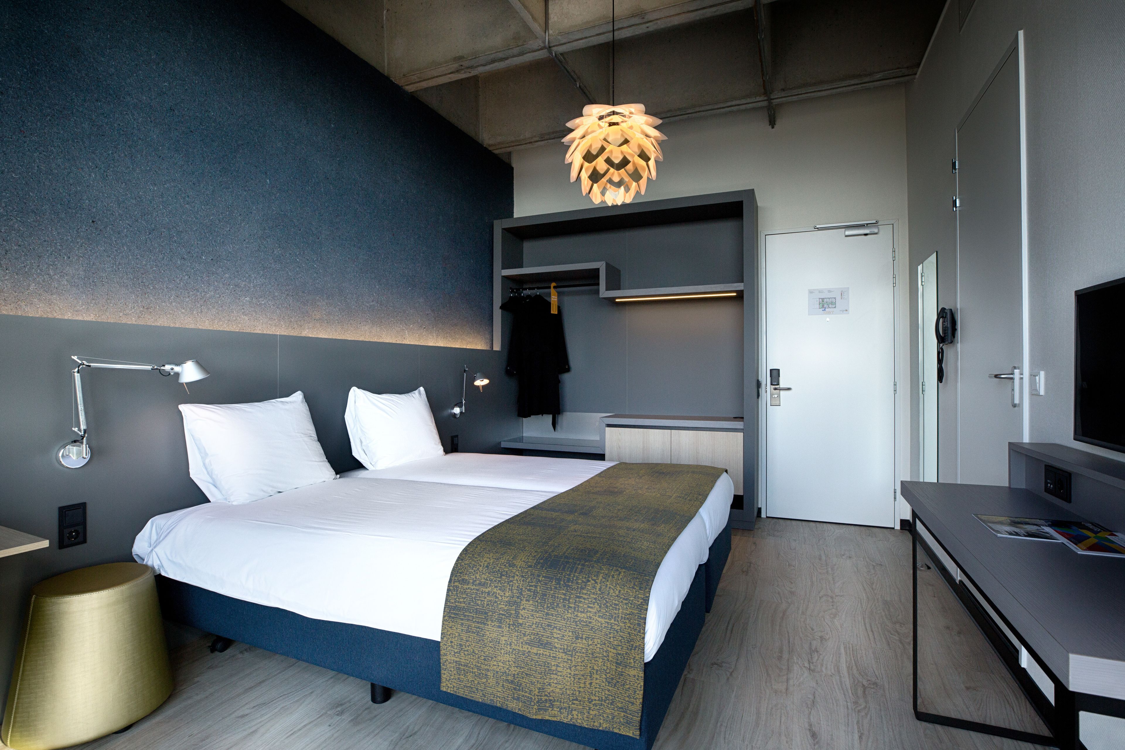 Una habitación de hotel moderna con una cama grande, mesitas de noche, un escritorio, televisión y una lámpara de techo original.