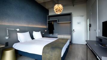 A modern hotel room with a large bed, bedside tables, a desk, a television, and a unique ceiling light fixture.