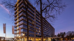 Un hotel de varios pisos con un diseño arquitectónico moderno, que cuenta con una entrada destacada y un amplio estacionamiento.