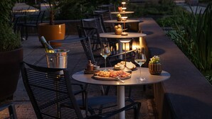 Un área de comedor al aire libre con mesas, sillas e iluminación ambiental.