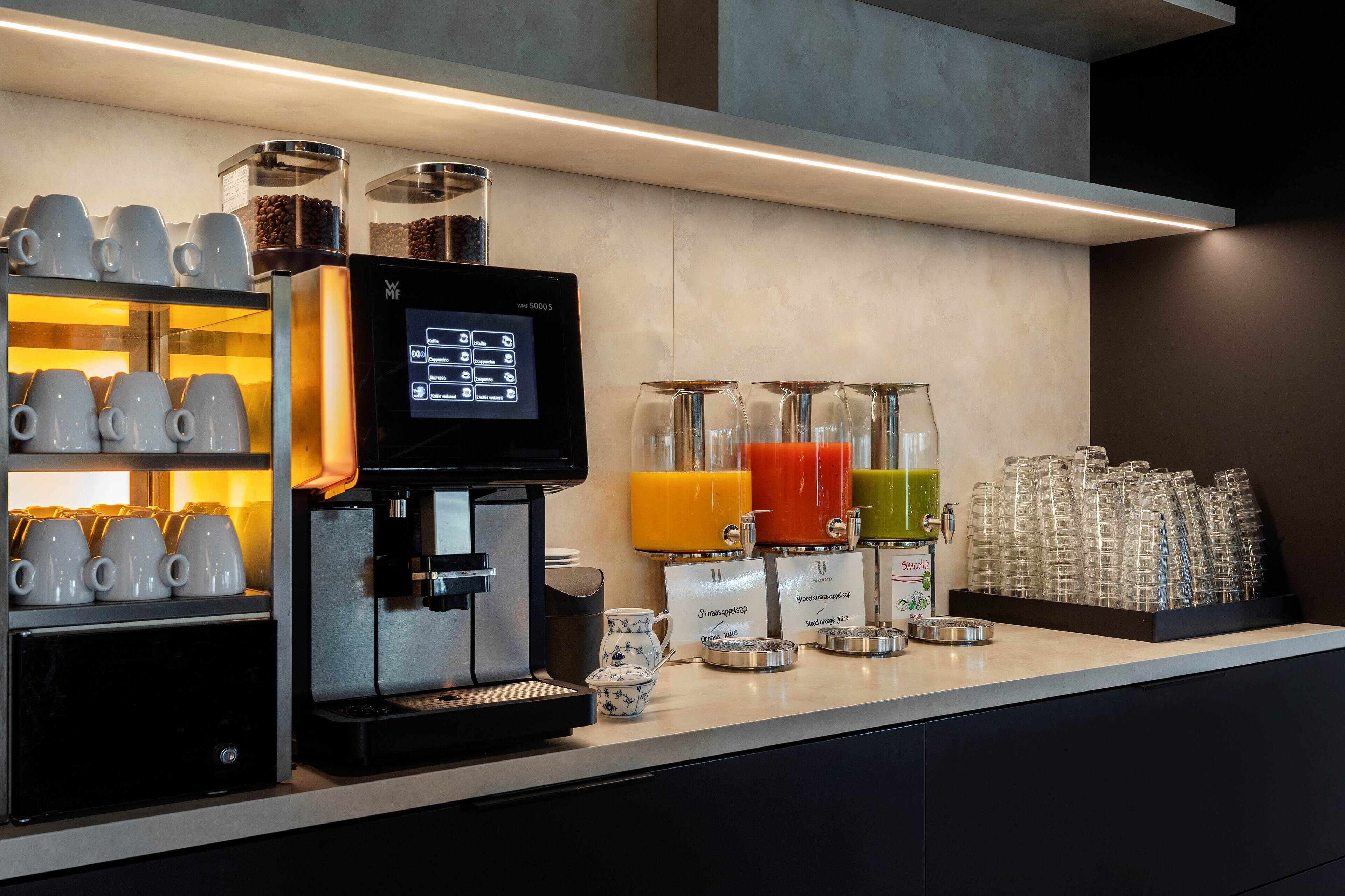 A coffee station with an espresso machine, coffee cups, and a juice dispenser.