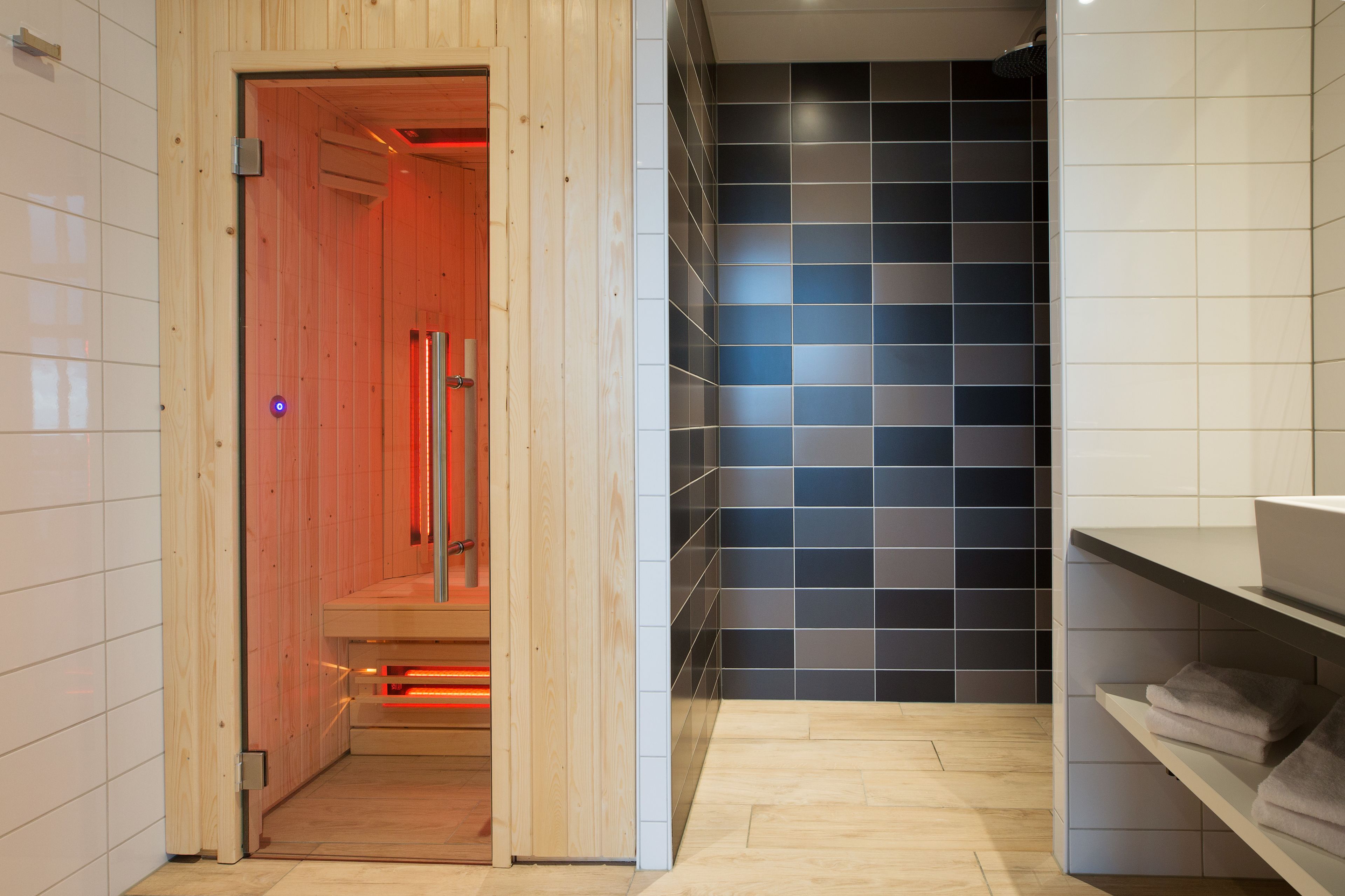 Un sauna con paredes de madera, piso de baldosas y un estante con toallas.
