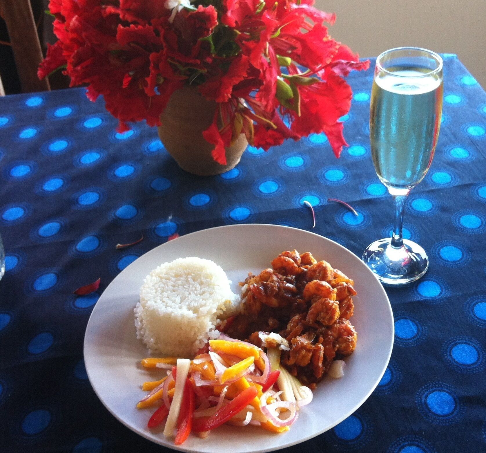 Un plato con arroz, pollo frito y una ensalada de vegetales sobre un mantel azul con estampado de lunares.