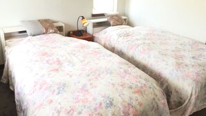 Un dormitorio con dos camas individuales, una mesita de noche con lámpara y un ventanal que deja entrar luz natural.