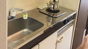 Una cocina con un lavamanos de acero inoxidable, una tetera y una estantería con tazas y una cafetera.