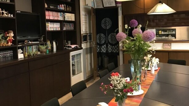 Un comedor moderno con una mesa larga, armarios de madera oscura y varios objetos decorativos, incluyendo un jarrón con flores.