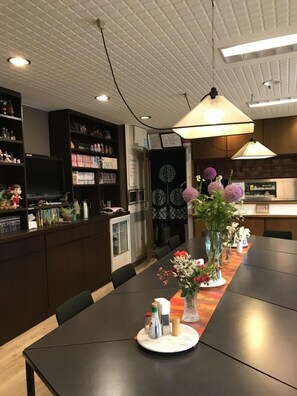 Un comedor moderno con una mesa larga, armarios de madera oscura y varios objetos decorativos, incluyendo un jarrón con flores.