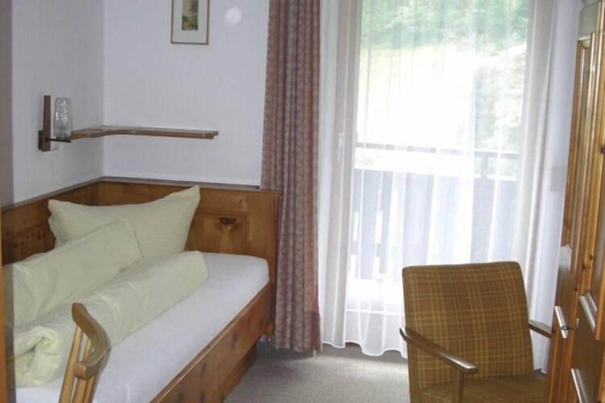 Un dormitorio con una cama de madera, una silla, una ventana con cortinas y un cuadro pequeño en la pared.