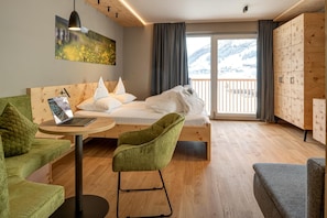 A hotel room with a bed, a desk with a laptop, green chairs, a painting, and a view of a snowy landscape.