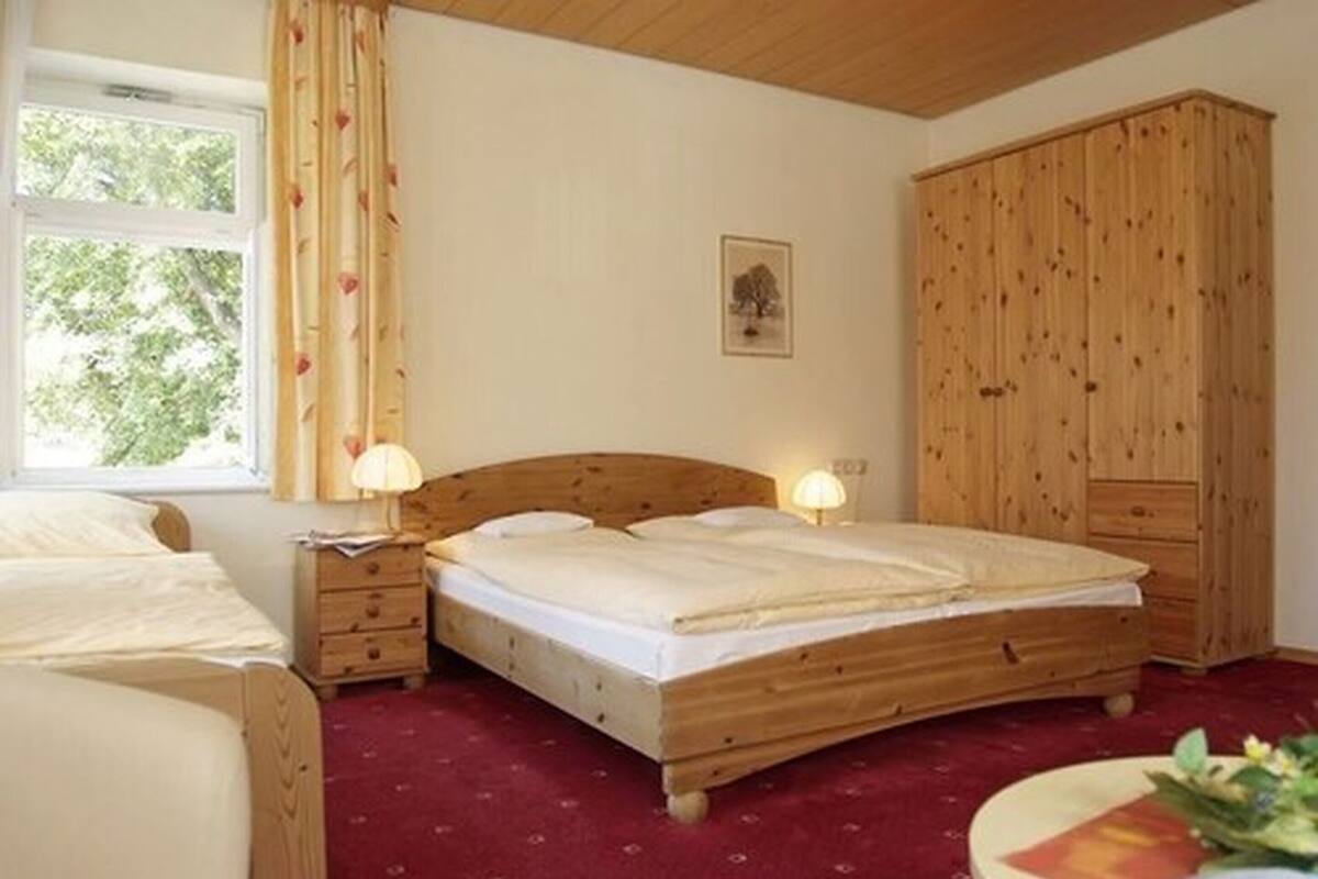 A bedroom with a wooden bed, a nightstand, a wardrobe, and a window with curtains.