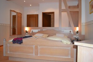 Quarto com uma cama grande, duas luminárias laterais, cabeceira de madeira e mesa de cabeceira com um telefone.