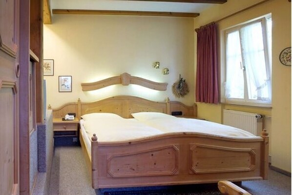 A wooden bed in a room with a window, a radiator, and a wall-mounted clock. - Hotel-Gasthof Rödertor (Rothenburg ob der Tauber)