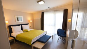 A hotel room with a bed, bedside lamps, a bench, a chair, and a large window with curtains. - Maurers Zollamt Hotel (Kaiserslautern)