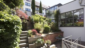 A garden with steps leading to a patio area, surrounded by various plants and a brick wall. - Maurers Zollamt Hotel (Kaiserslautern)