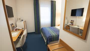 Quarto de hotel com cama, escrivaninha com cadeira, luminária de mesa, telefone, cafeteira e televisão fixada na parede.