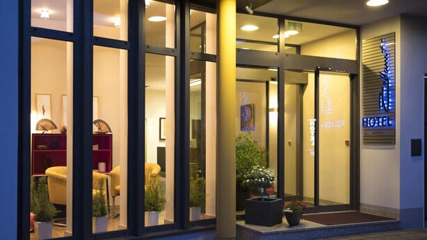 A hotel entrance with glass doors, a reception desk, and potted plants. - Maurers Zollamt Hotel (Kaiserslautern)