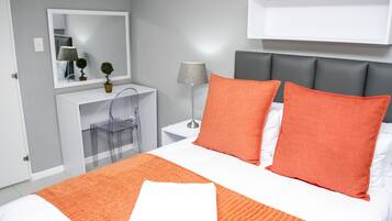 A neatly arranged hotel room with a bed, a bedside table, a lamp, a mirror, and a small desk with a chair.