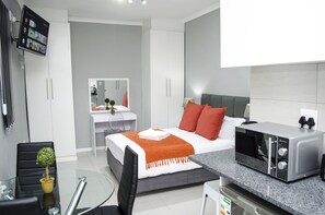 Une chambre moderne équipée d’un lit, d’un bureau, d’une chaise, d’un four à micro-ondes et d’une télévision.