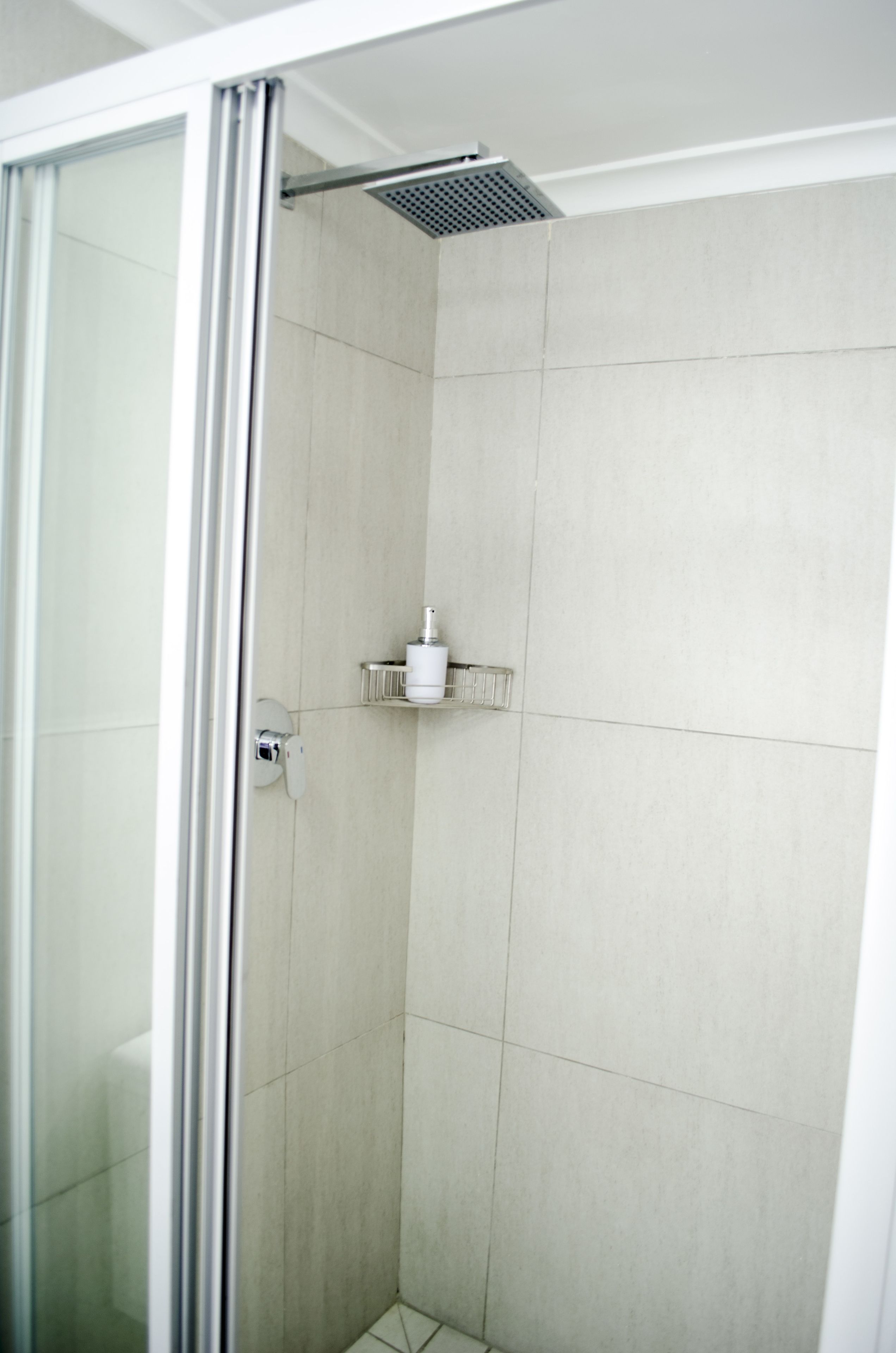A modern bathroom with a glass shower enclosure, a white toilet, and a small shelf with toiletries.