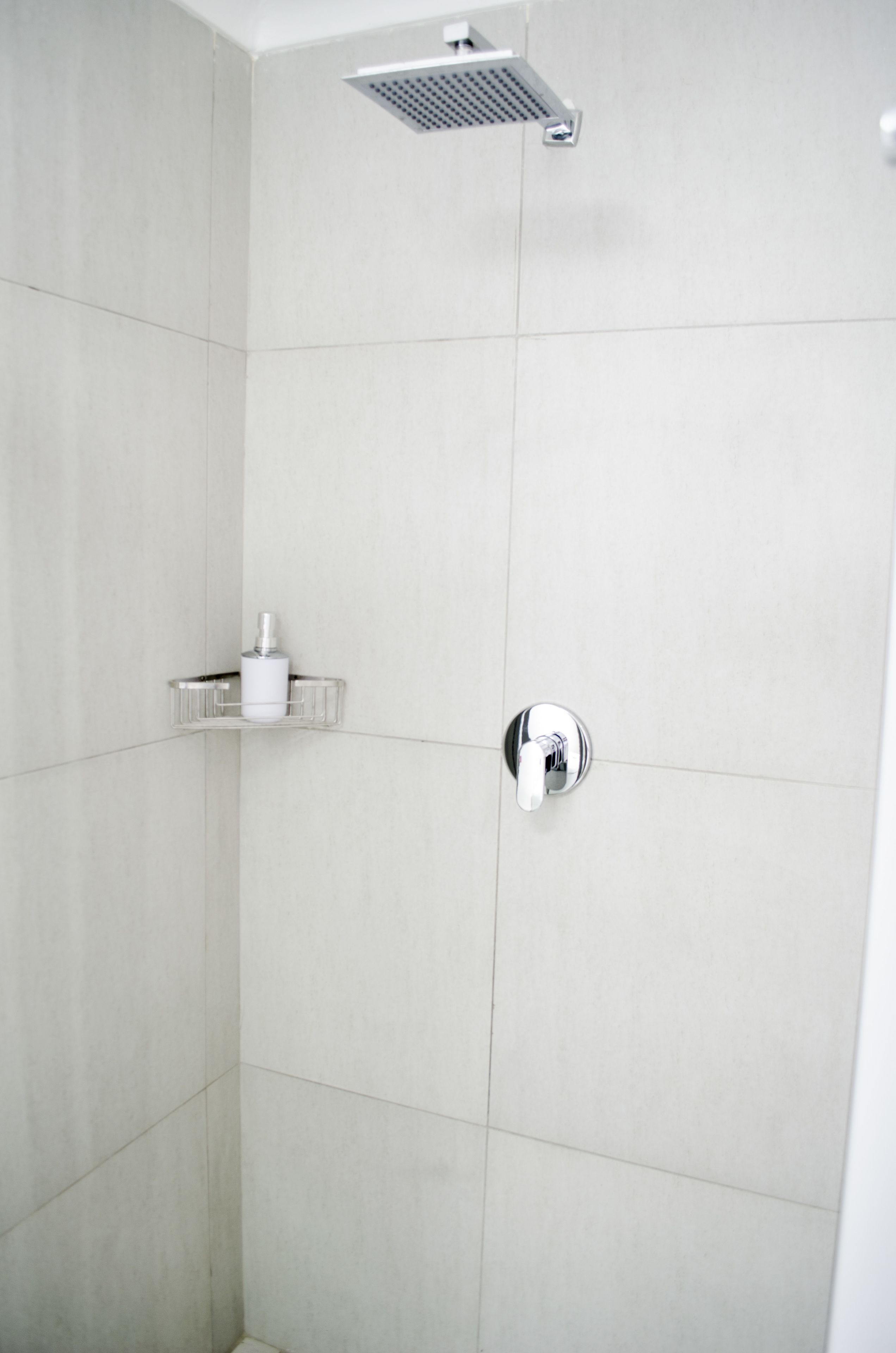 A shower with a chrome faucet and a soap holder on a wall.