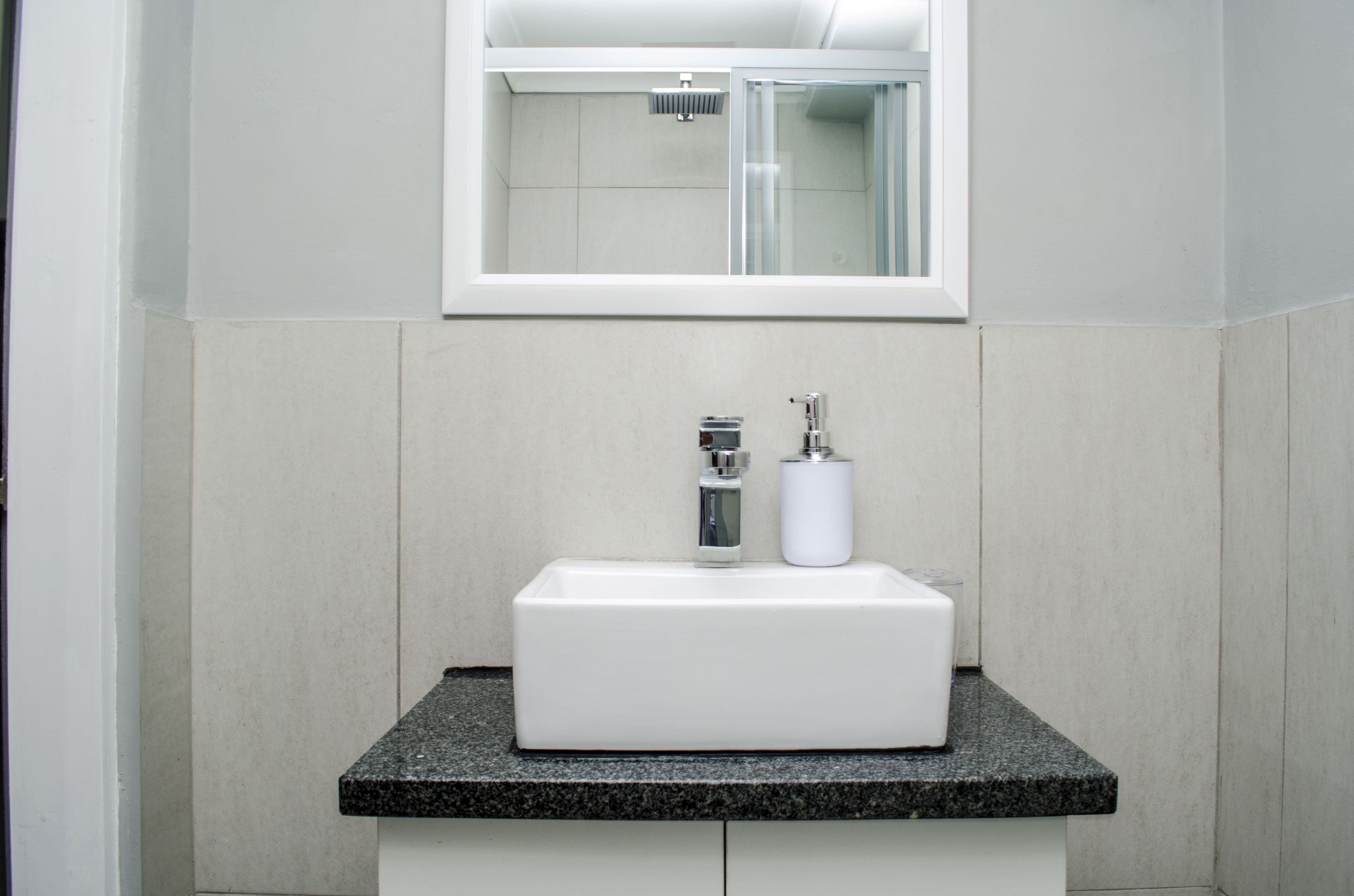 Un baño con lavamanos blanco, espejo y ducha.