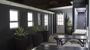A covered outdoor area with potted plants, a wooden bench, and a door leading to another section. - Cape Town Micro Apartments (Cape Town)