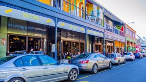 A street with parked cars and a building with multiple storefronts, including OBZ CAFE. - Cape Town Micro Apartments (Cape Town)