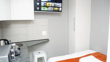Une petite chambre moderne, équipée d’un lit, d’un téléviseur fixé au mur, d’un lavabo et d’un petit tabouret.