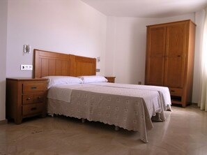 Een slaapkamer met een houten bed, nachtkastje, kledingkast en een stopcontact.