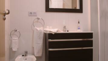 Un baño con un lavamanos blanco pedestal, un tocador negro con espejo y un perchero para toallas.