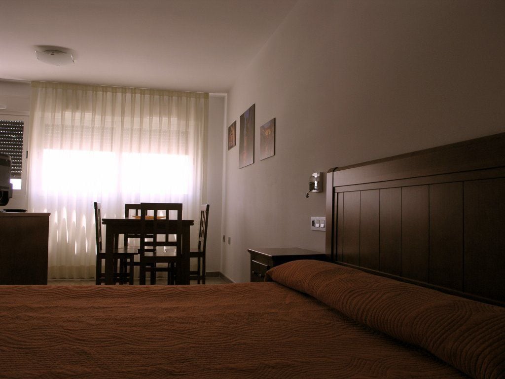 Una habitación de hotel con una cama grande, un escritorio con silla, una ventana con cortinas y un cabecero.