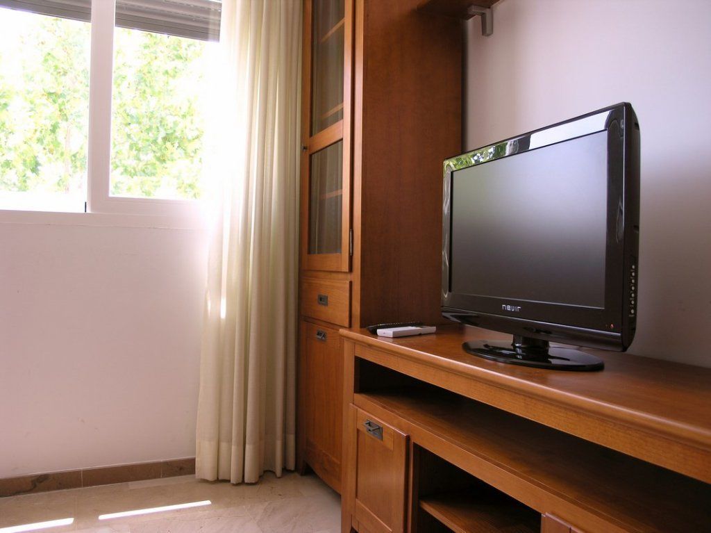 Un escritorio de madera con un televisor de pantalla plana, una ventana con cortinas y una puerta.