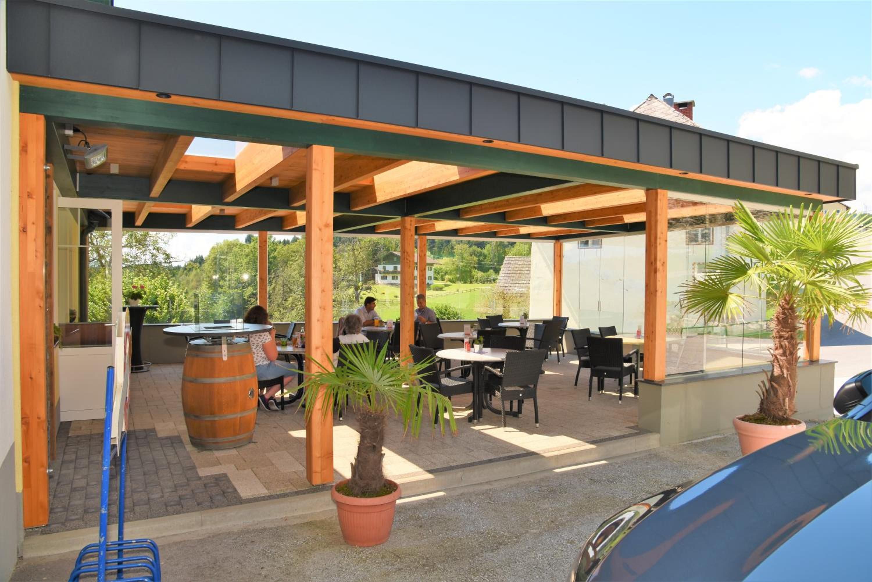 An outdoor patio area with wooden beams, tables, chairs, and potted plants.