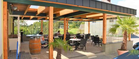 An outdoor patio area with wooden beams, tables, chairs, and potted plants.