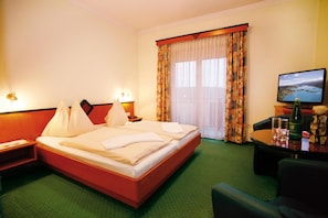 A hotel room with a bed, a desk, a chair, a television, and a window with curtains.