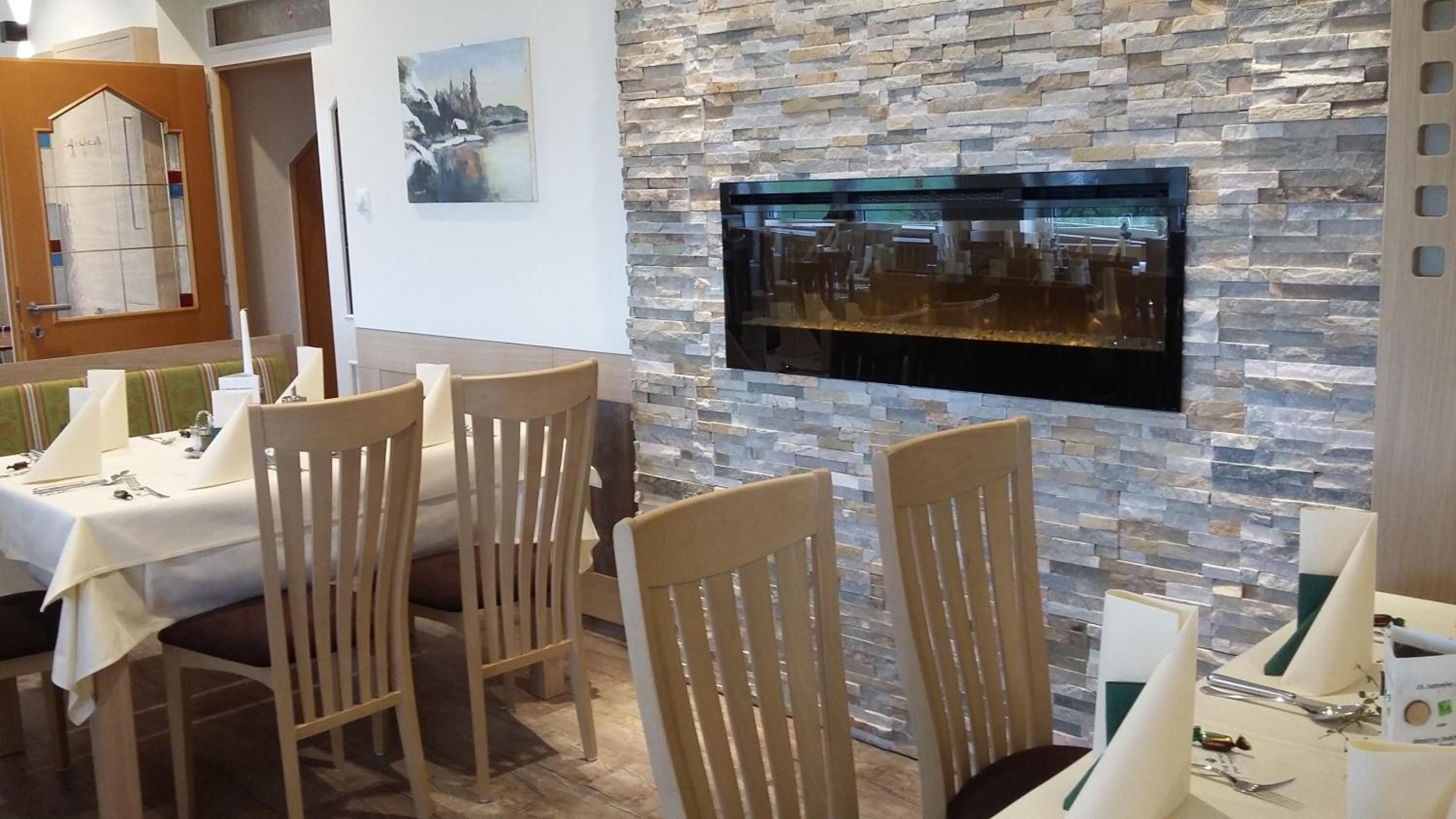 A dining area with a stone wall, a flat-screen TV mounted on it, and a table set for a meal.