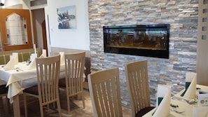 A dining area with a stone wall, a flat-screen TV mounted on it, and a table set for a meal.